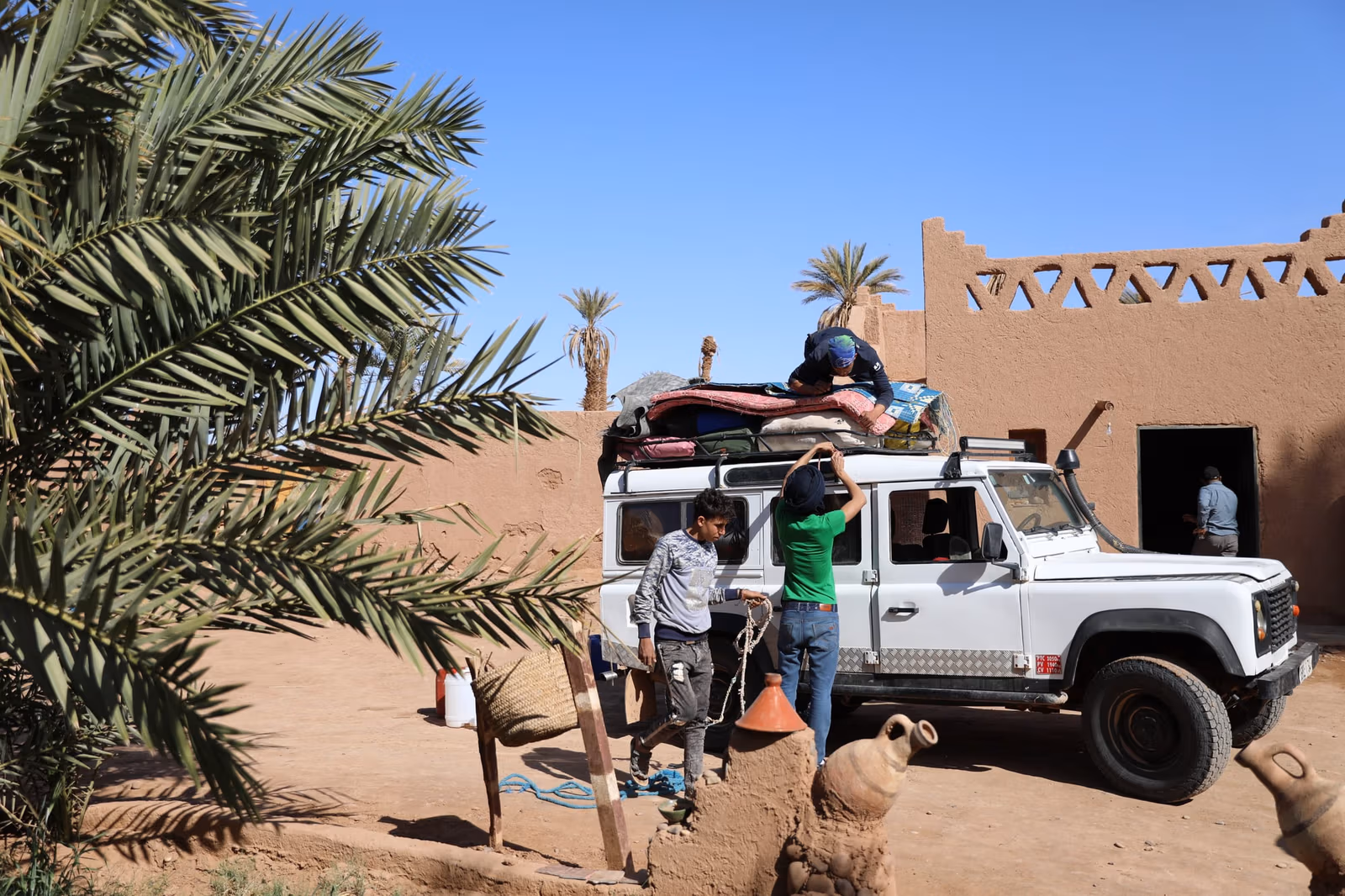 A loaded vehicle on a desert track beside a kasbah and palm grove