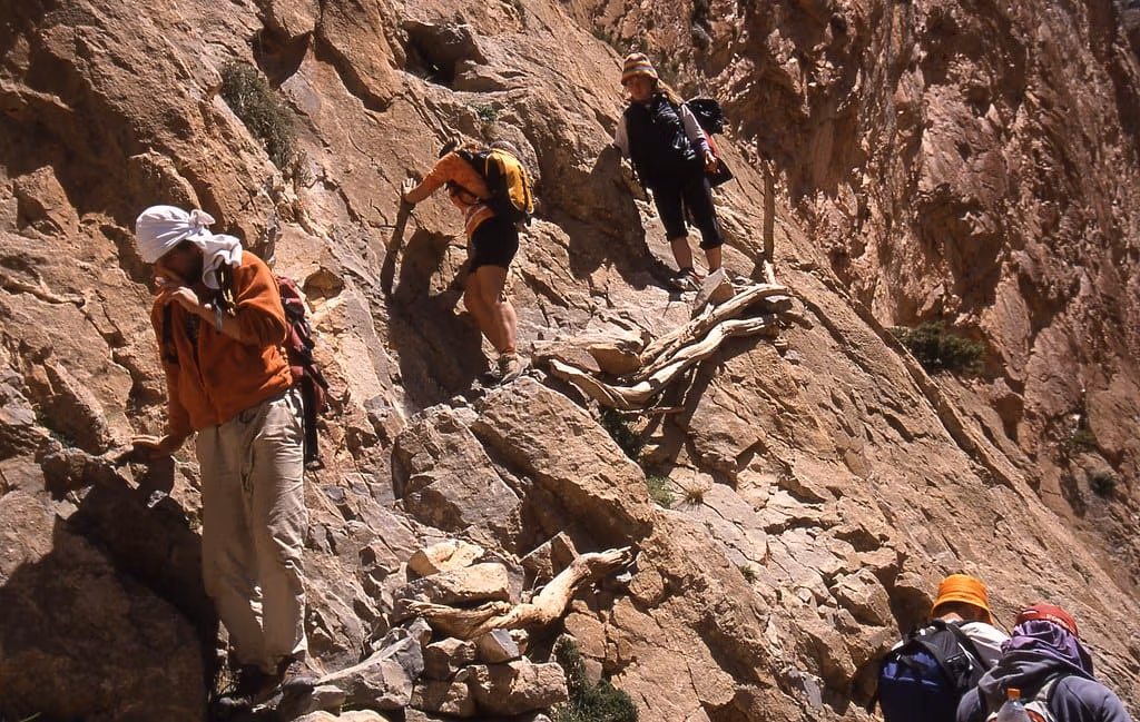 Trekkers scrambling up a steep rock path in the Taghia cirque